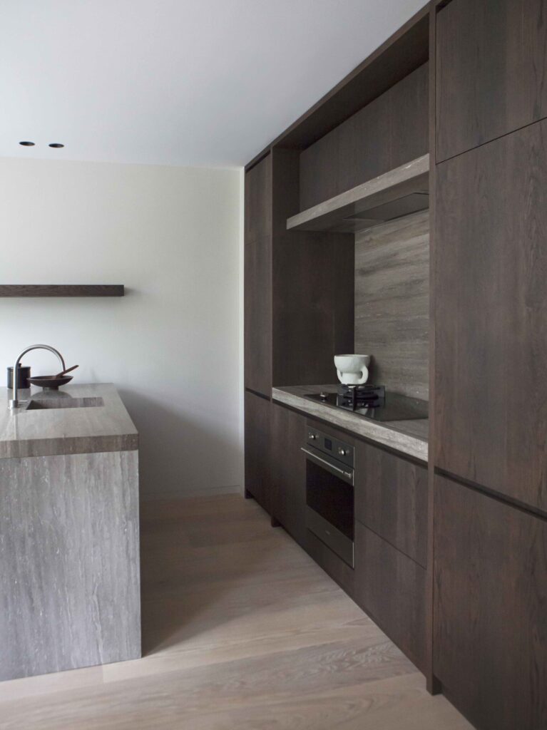 Kitchen in City Apartment Amsterdam defined by dark wood cabinetry, natural stone surfaces and restrained lines, forming a calm and architectural composition.